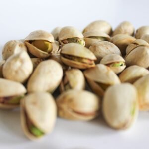 dry fruits and seeds A close-up of fresh pistachio nuts scattered on a white surface, showcasing their natural shells and vibrant color.