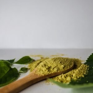 Image showcasing a close-up of herbal powder on a wooden spoon surrounded by green leaves.