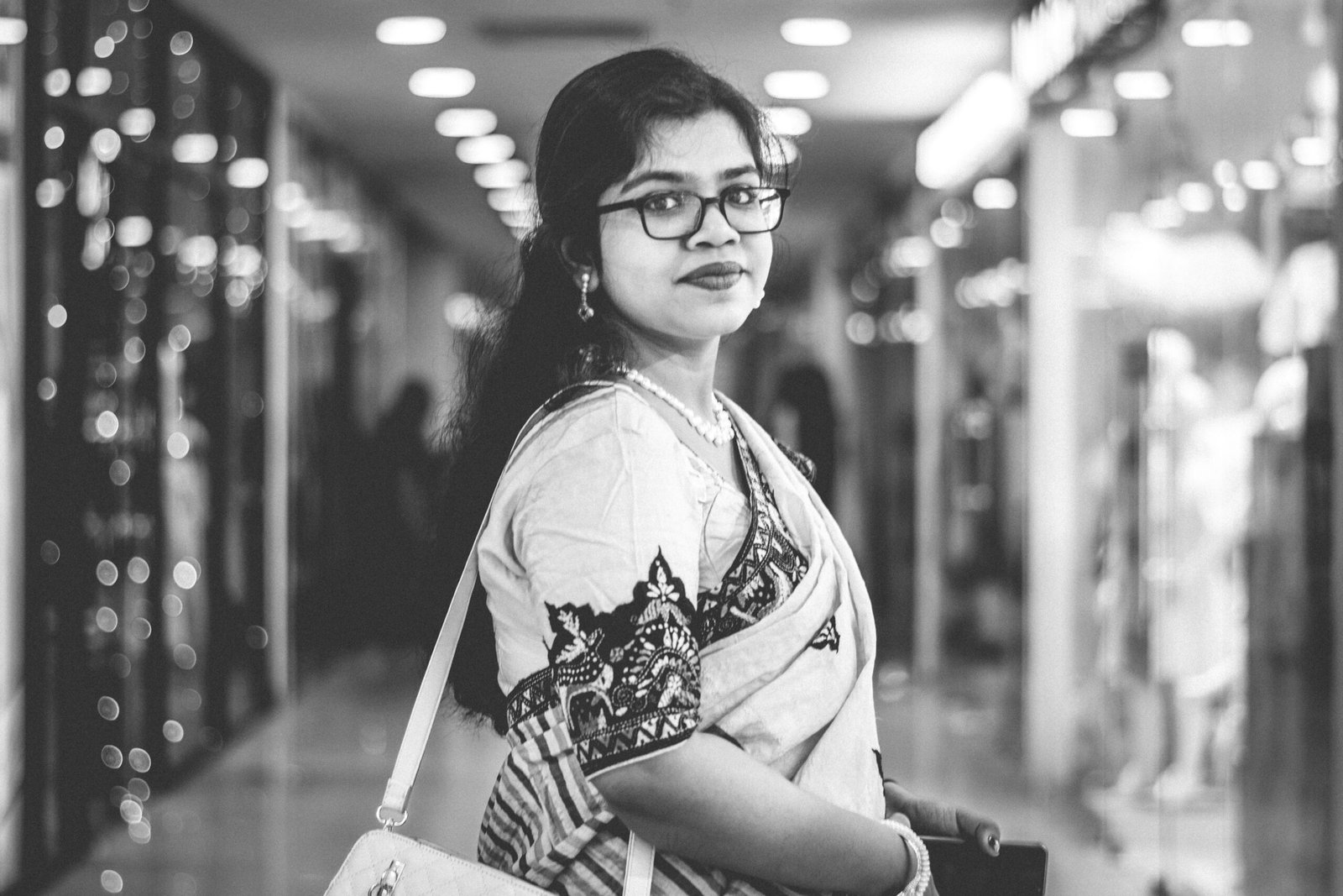 Black and white portrait of a woman in traditional attire shopping in a modern mall.
