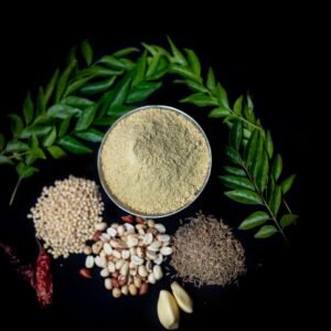 Flat lay of Indian spices and curry leaves on black. Includes cumin, garlic, peanuts, and more.