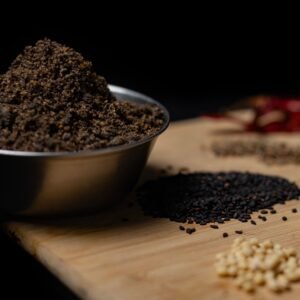 Close-up of assorted spices including black sesame and garlic on a wooden board.