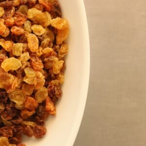 dry fruits and seeds Close-up of assorted yellow and brown raisins in a white bowl on a textured background.