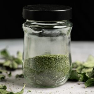 Close-up of a glass jar filled with dried, powdered mint leaves, ideal for culinary use.