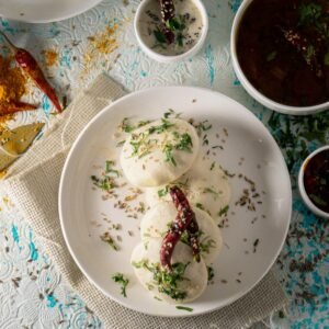 Top view of delicious Idli rice cakes with herbs and spicy tomato soup served on table near sauces and scattered spices