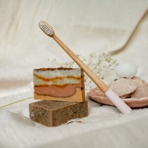 Sustainable bath essentials including soaps and a bamboo toothbrush on a textile surface.