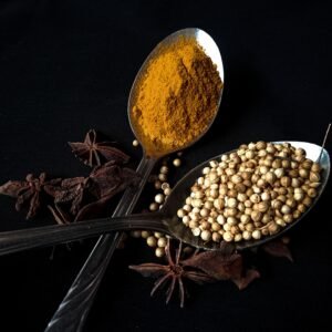 Top view of turmeric and coriander with star anise on spoons, against a black backdrop.