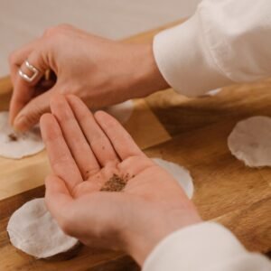 Hands creating seed bombs using cotton pads and seeds on a wooden surface, promoting eco-friendly gardening.