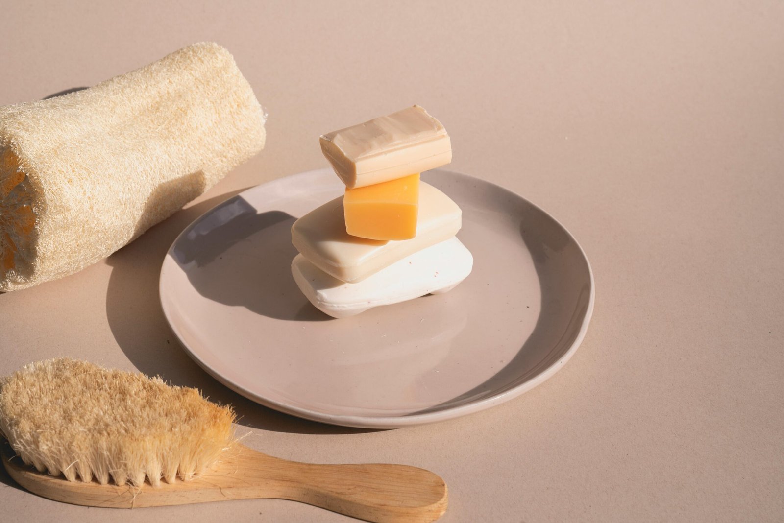 Artistic arrangement of various soaps on a plate with loofah and brush.