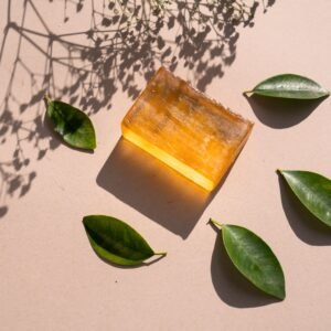 Flat lay of a natural soap bar with green leaves and shadows on a beige surface.
