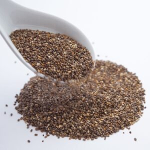 dry fruits and seeds A close-up shot of chia seeds pouring from a white ceramic spoon onto a white surface.