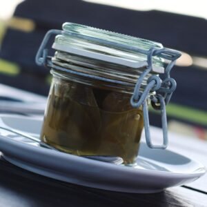 A detailed close-up shot of pickled jalapenos in a glass jar on a white plate outdoors.
